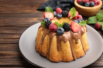 Tasty Bundt cake with berries, chocolate and mint on wooden table, closeup