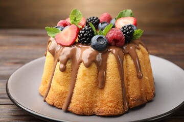 Tasty Bundt cake with berries, chocolate and mint on wooden table, closeup