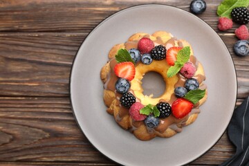 Tasty Bundt cake with berries, chocolate and mint on wooden table, top view. Space for text