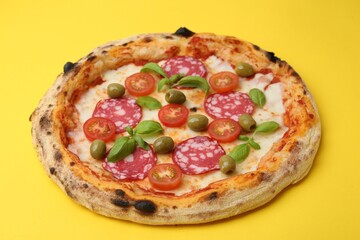 Delicious pizza with salami, olives, tomatoes and basil on yellow table, closeup