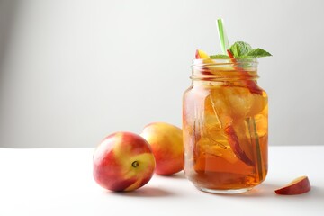 Refreshing iced peach tea with mint in mason jar and fresh fruits on white table, closeup. Space...