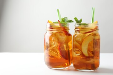 Refreshing iced peach tea with mint in mason jars on white table, closeup. Space for text