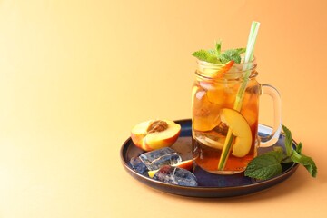 Refreshing iced peach tea with mint in mason jar on pale orange background, space for text