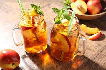 Refreshing iced peach tea with mint in mason jars and fresh fruits on wooden table, closeup