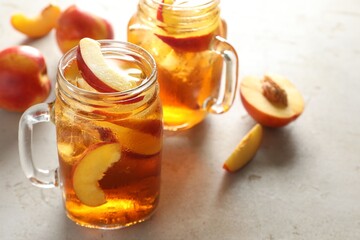 Refreshing iced peach tea in mason jars on light table, closeup