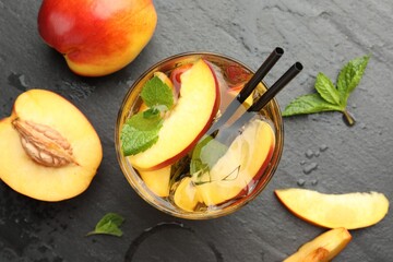 Refreshing iced peach tea in glass and fresh fruits on dark table, flat lay