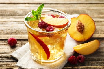 Iced tea. Refreshing drink with peach and raspberries in glass on wooden table, closeup