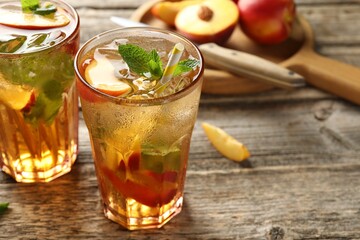 Refreshing iced peach tea in glasses and fresh fruits on wooden table, closeup