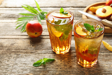 Refreshing iced peach tea in glasses and fresh fruits on wooden table, closeup