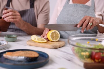 Elderly couple cooking together at white marble table indoors, closeup