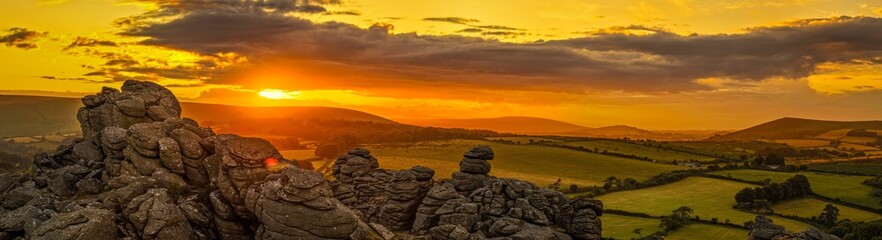 Family hiking on Dartmoor tors at sunset, silhouetted against dramatic skies in scenic moorland...