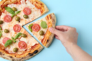 Woman taking piece of delicious pizza at light blue table, top view