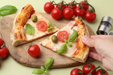 Woman taking piece of delicious pizza at light green table, closeup
