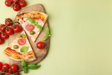 Pieces of delicious pizza, tomatoes and basil on light green background, flat lay. Space for text