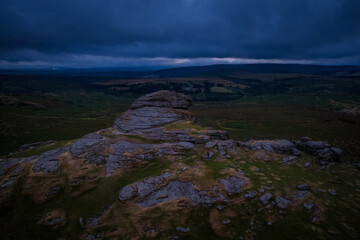Family hiking on Dartmoor tors at sunset, silhouetted against dramatic skies in scenic moorland landscape