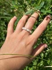 Hand resting on green grass in macro view with pearl ring on finger and natural summer texture