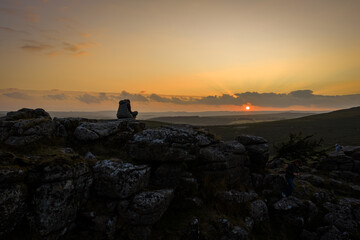 Family hiking on Dartmoor tors at sunset, silhouetted against dramatic skies in scenic moorland...