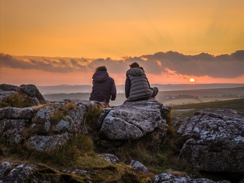 Family hiking on Dartmoor tors at sunset, silhouetted against dramatic skies in scenic moorland landscape