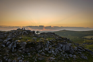 Family hiking on Dartmoor tors at sunset, silhouetted against dramatic skies in scenic moorland...