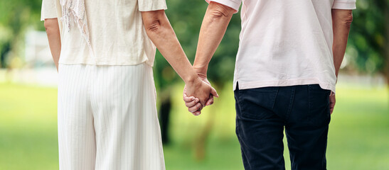 Senior couple walking hand in hand together outdoors enjoying tranquil park nature leisurely pace...