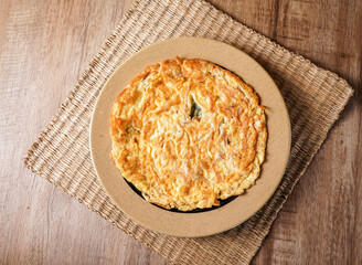 Golden brown anchovy omelette on a rustic wooden table in plate side view of Asian food