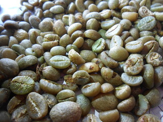 A pile of raw, unroasted coffee beans. The beans have a natural green and brown color, highlighting the initial process of coffee production. This image is perfect for themes related to coffee