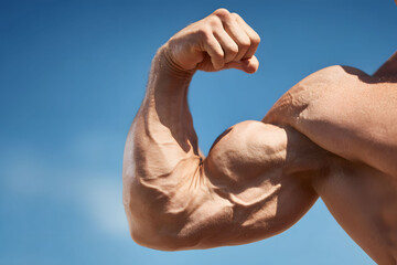 Close Up Of A Muscular Man's Flexed Arm Against A Blue Sky