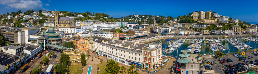 Fototapeta premium Aerial view of Torquay Marina on a sunny day, featuring yachts, boats, promenade, and blue sea along the English Riviera coastline
