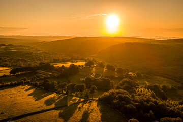 Golden sunrise over the rocky tors of Dartmoor, casting warm light across the rugged moorland and...