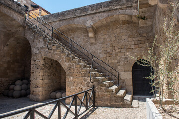 Historic stone courtyard with arched staircases, ancient sculptures in a Mediterranean old town