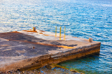 Weathered concrete pier stretches into still water, its surface marked by age and scattered debris....