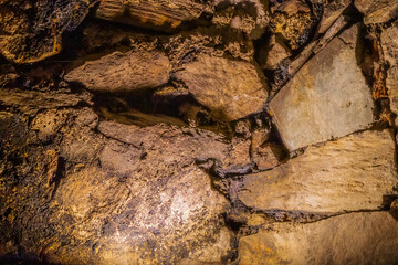 Close-up of rough ancient stone wall with golden lighting in archaeological interior