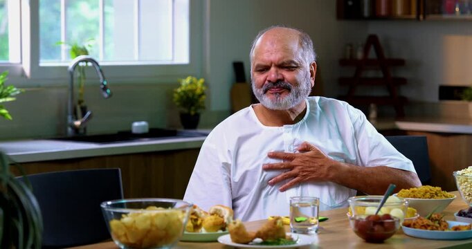 Senior Indian man drinking antacid in modern kitchen, Asian elderly person experiencing acidity or indigestion after food, taking antacid liquid to ease discomfort and feel better at home