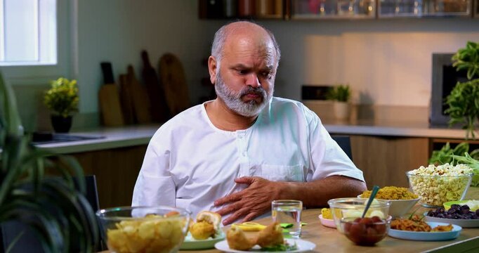 Senior Indian man drinking antacid in modern kitchen, Asian elderly person experiencing acidity or indigestion after food, taking antacid liquid to ease discomfort and feel better at home