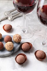Delicious truffle bonbons and red wine on light grey background, closeup
