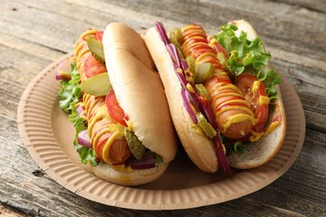 Tasty hot dogs with vegetables, mustard and ketchup on wooden table, closeup