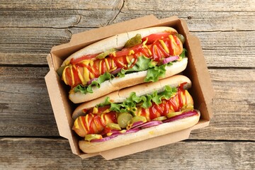 Tasty hot dogs with vegetables, mustard and ketchup on wooden table, top view