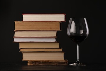 Red wine in glass and stack of books on table against black background, closeup