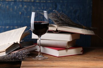 Red wine in glass, lavender flowers and books on wooden table against blue background, closeup