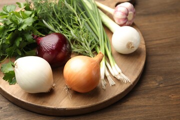 Different fresh herbs, onions and garlic on wooden table, closeup