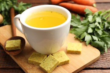 Aromatic bouillon cubes, broth, parsley and vegetables on wooden table, closeup