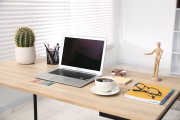 Modern laptop, coffee and stationery on wooden desk in office. Comfortable workplace
