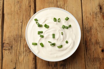 Tasty sour cream with green onions in bowl on wooden table, top view