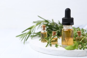 Bottles of essential oil and herbs on white tiled table, closeup. Space for text