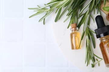 Bottles of essential oil and herbs on white tiled table, flat lay. Space for text