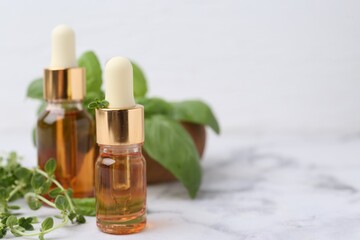Bottles of essential oil and herbs on white marble table, closeup. Space for text