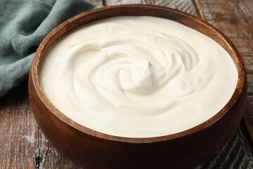 Delicious sour cream in bowl on wooden table, closeup