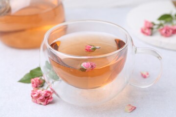 Aromatic tea in glass cup and roses on light table, closeup