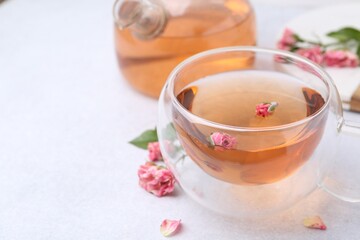 Aromatic tea in glass cup, teapot and roses on light table, closeup. Space for text