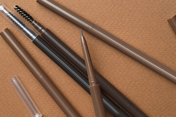 Different eyebrow pencils on brown background, flat lay